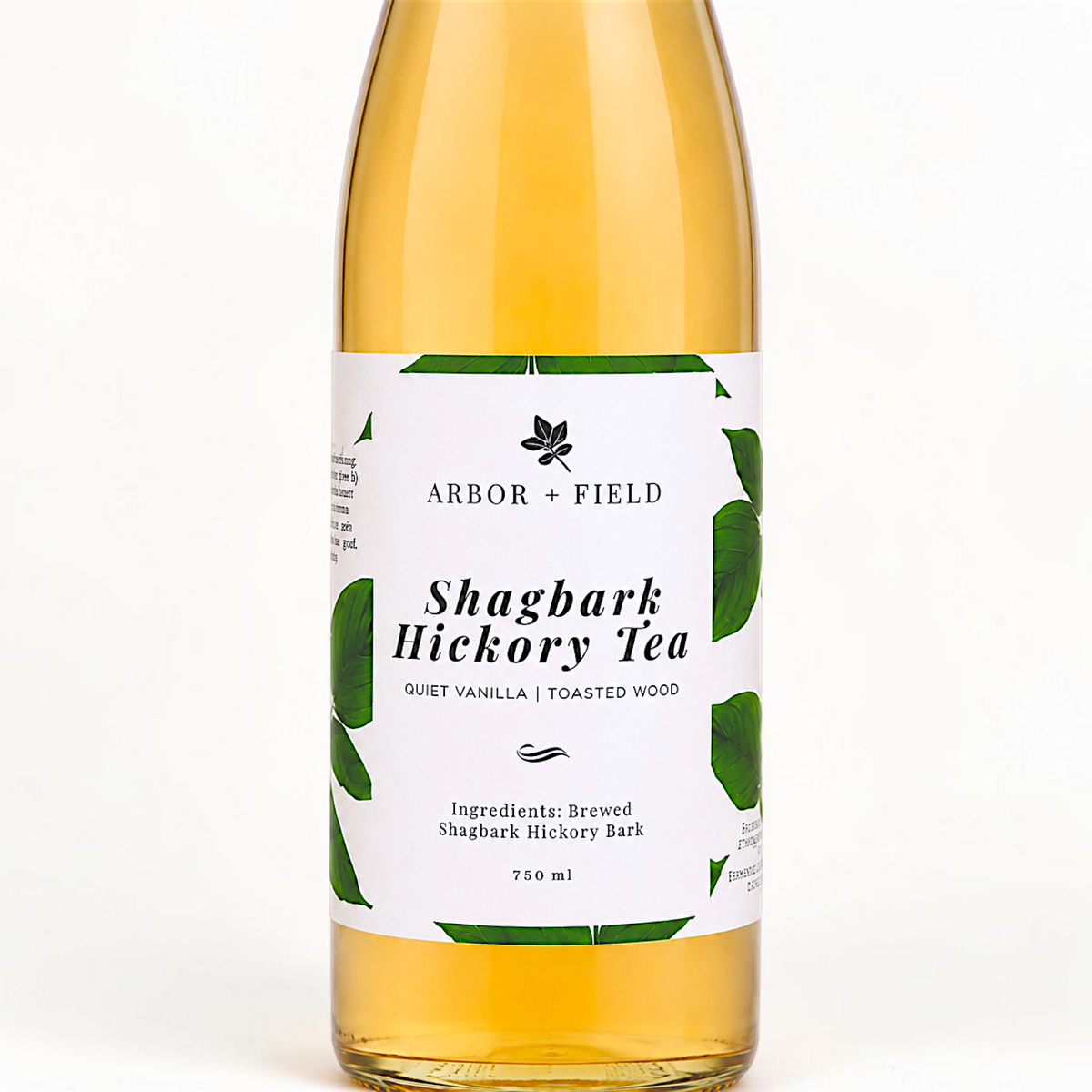 Bottle of Arbor and Field shagbark hickory tea with a green and white label. Modern clear glass wine bottle with amber colored tea inside. Clean white background, premium look and feel.