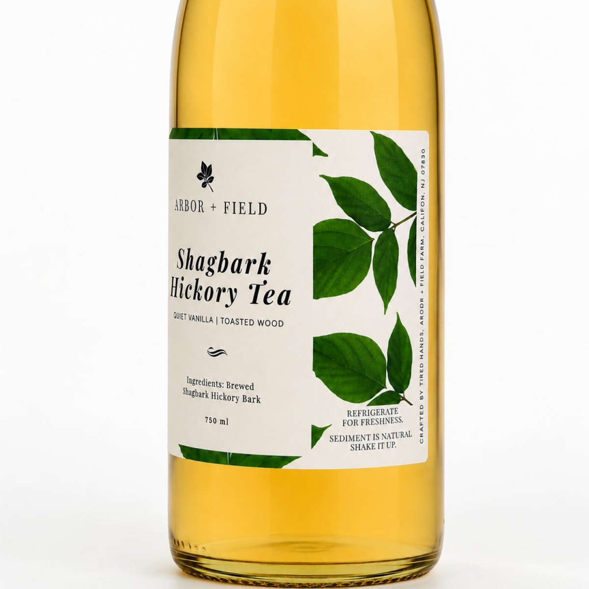 Bottle of Arbor and Field shagbark hickory tea with a green and white label. Modern clear glass wine bottle with amber colored tea inside. Clean white background, premium look and feel.