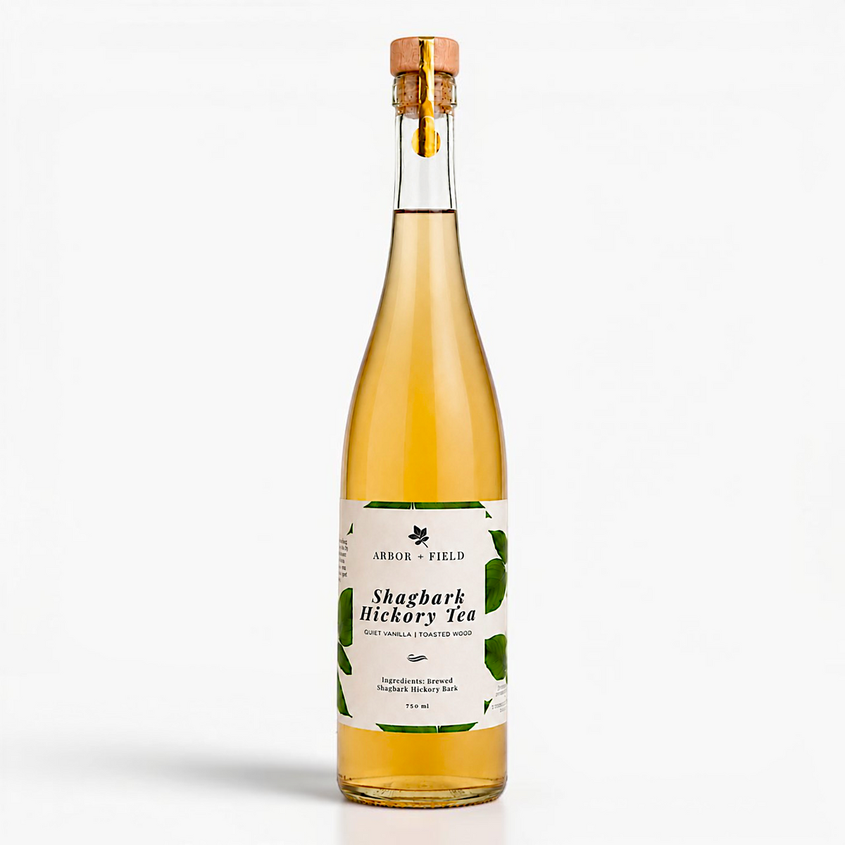 Bottle of Arbor and Field shagbark hickory tea with a wooden cork and green and white label. Modern clear glass wine bottle with amber colored tea inside. Clean white background, premium look and feel. 